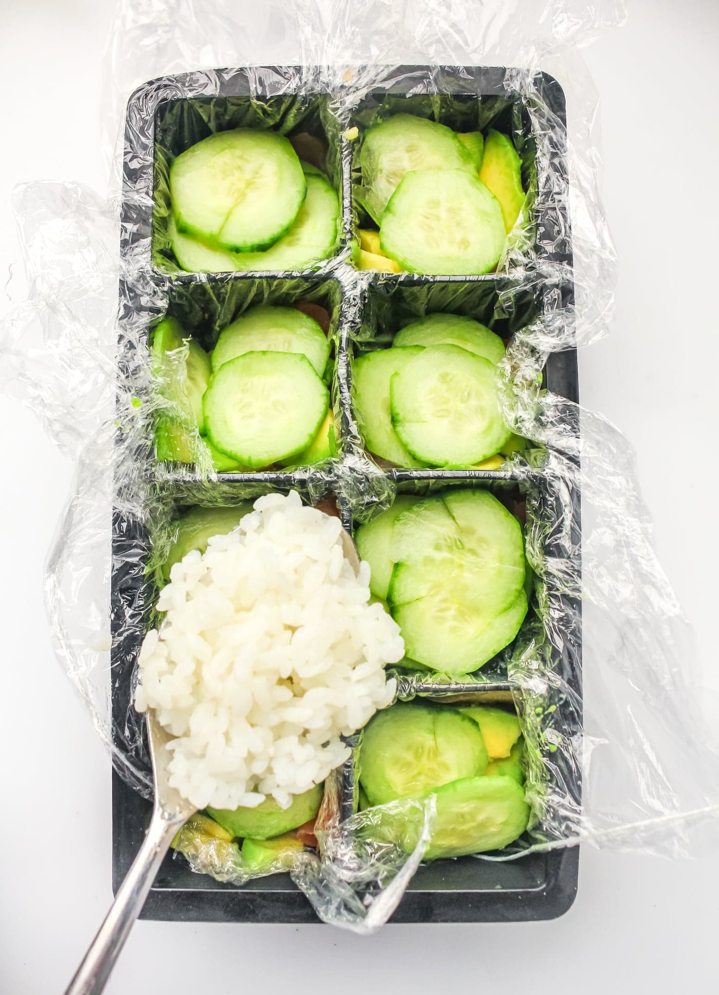 a spoon full of rice held over an ice cube tray for ice cube tray sushi salmon rolls