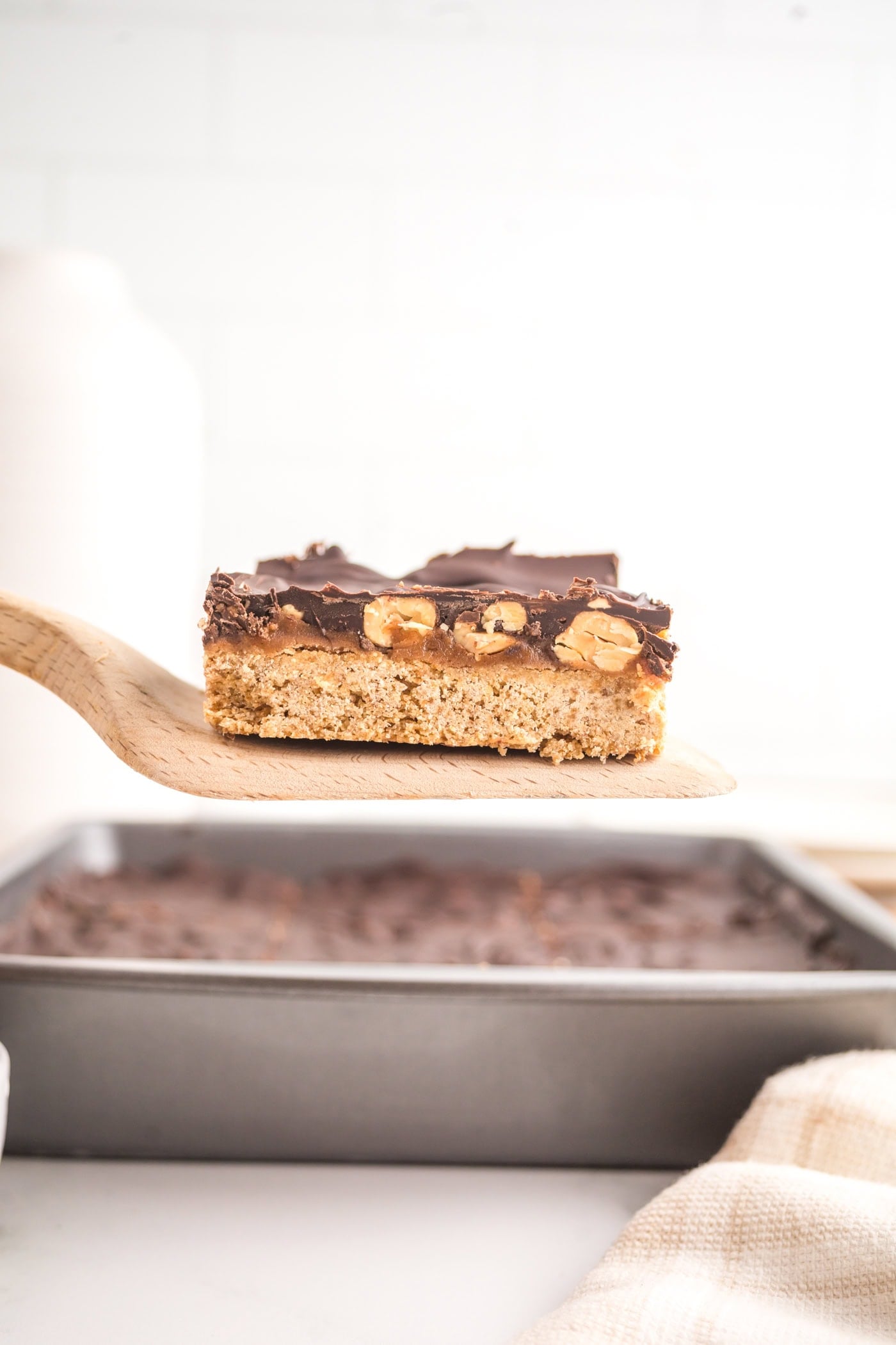 lifting a square of dairy free healthy snickers bars out of a pan