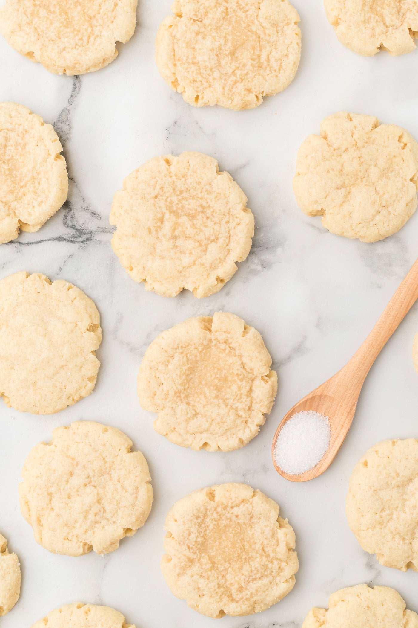 a stop down photo of sourdough discard sugar cookies on a white marble surface with a spoon of sugar