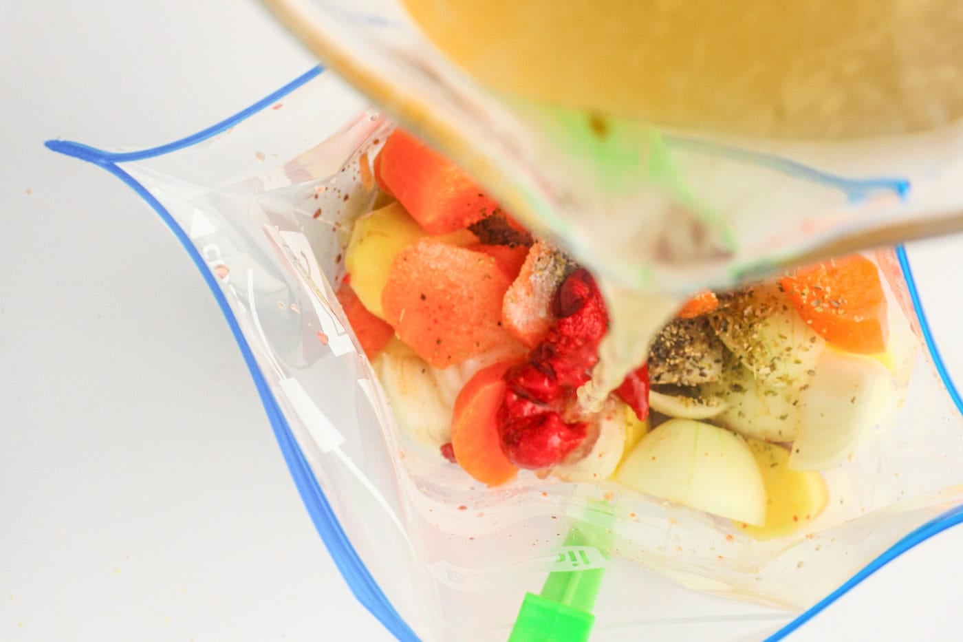 Pouring broth on top of vegetables and seasonings in a gallon freezer bag