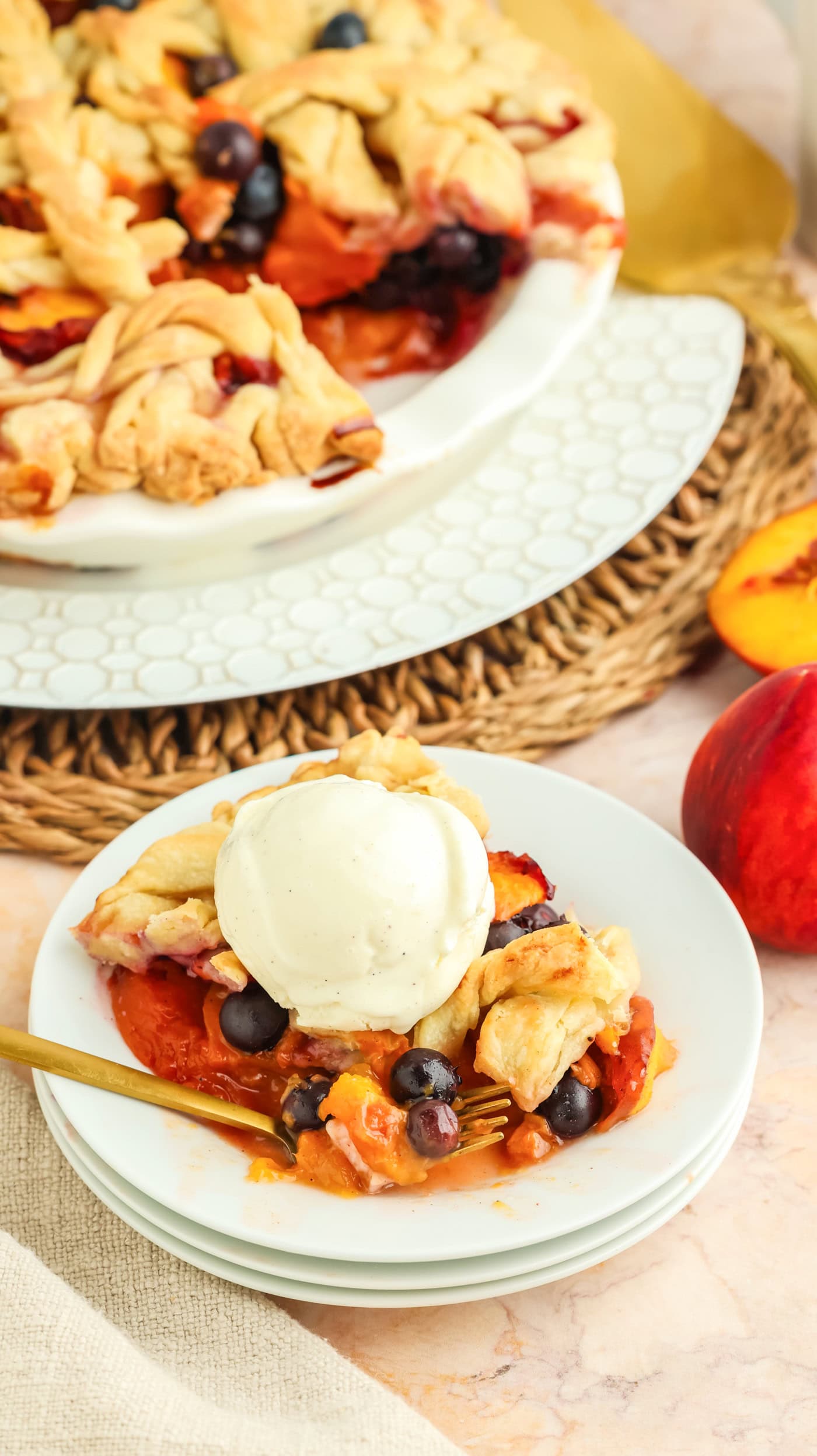 a slice of blueberry peach pie with a school of vanilla ice cream on top