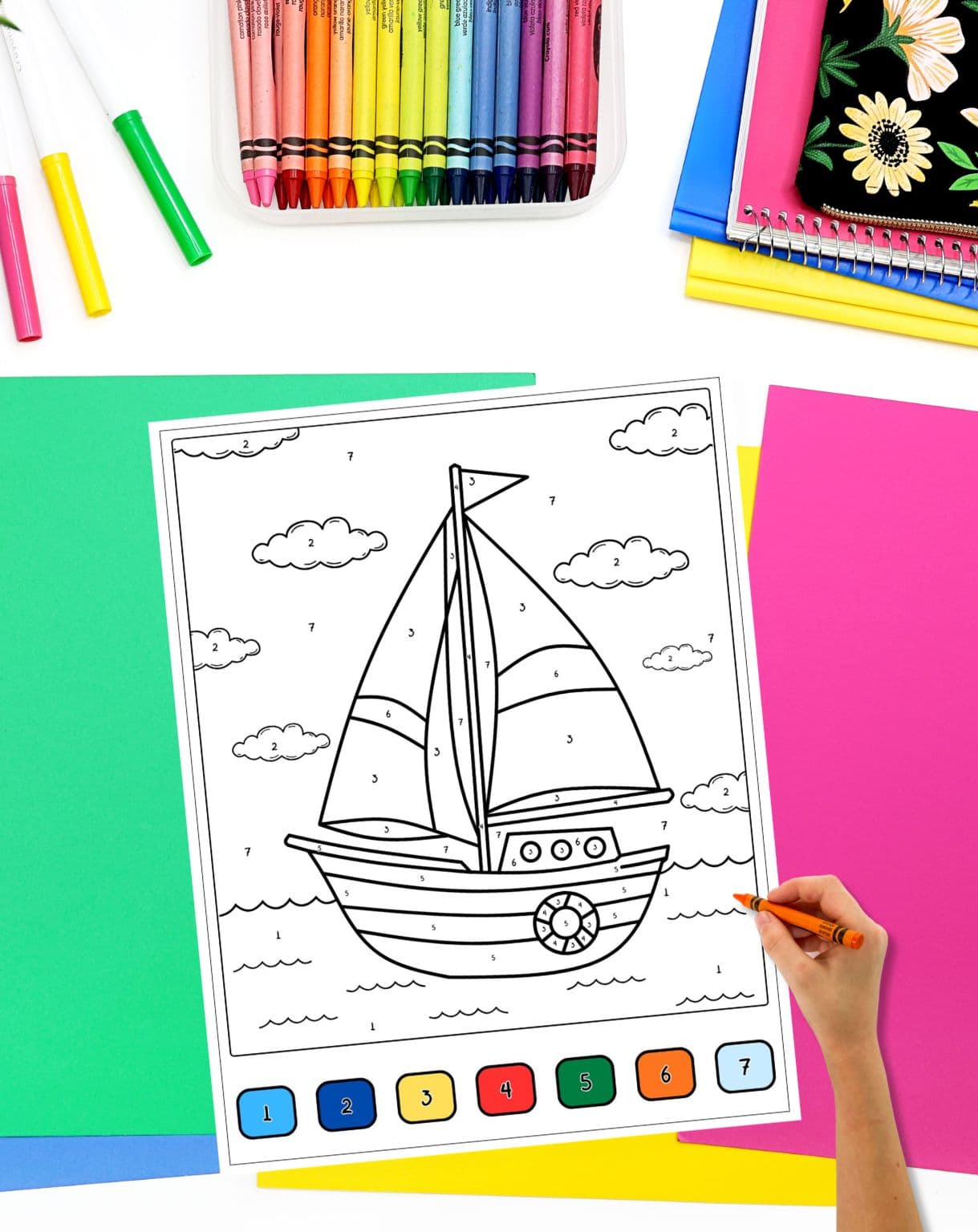 a hand with a crayon preparing to color a color by number sheet with a sailboat