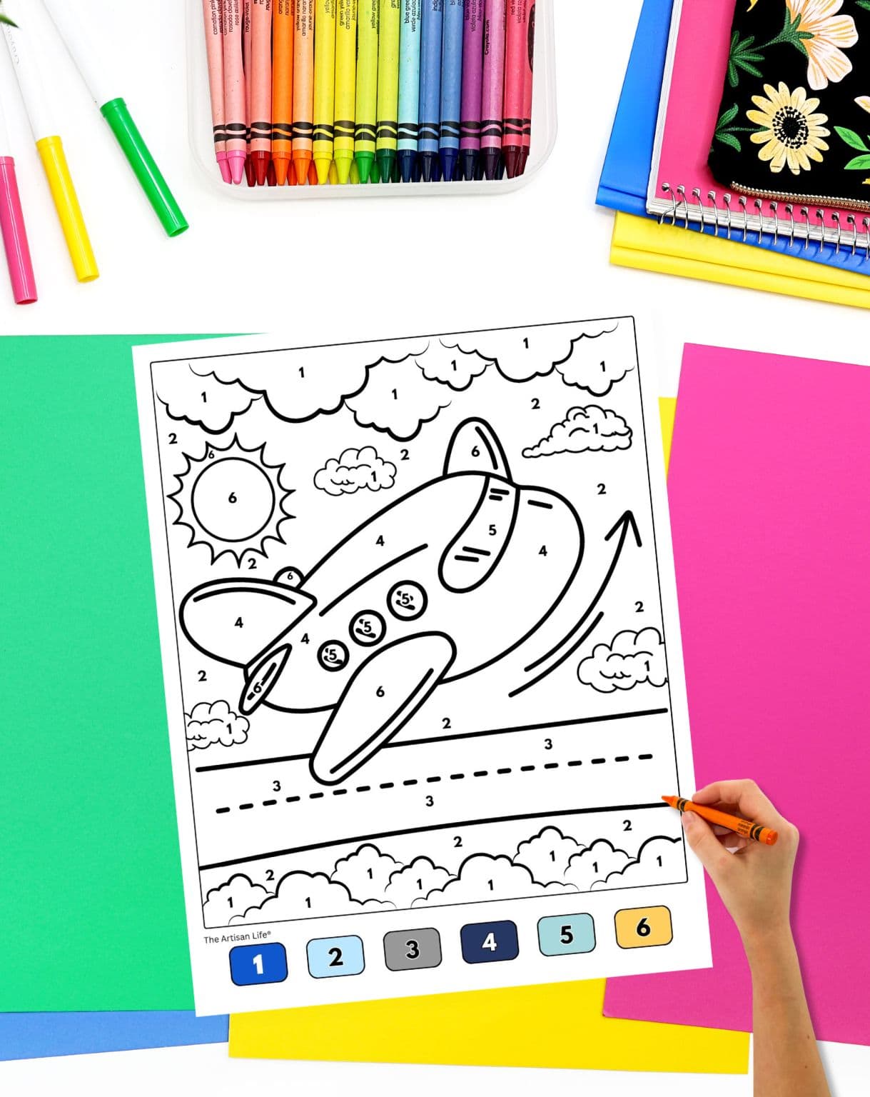 a hadn't holding an orange crayon preparing to color an airplane color by number sheet