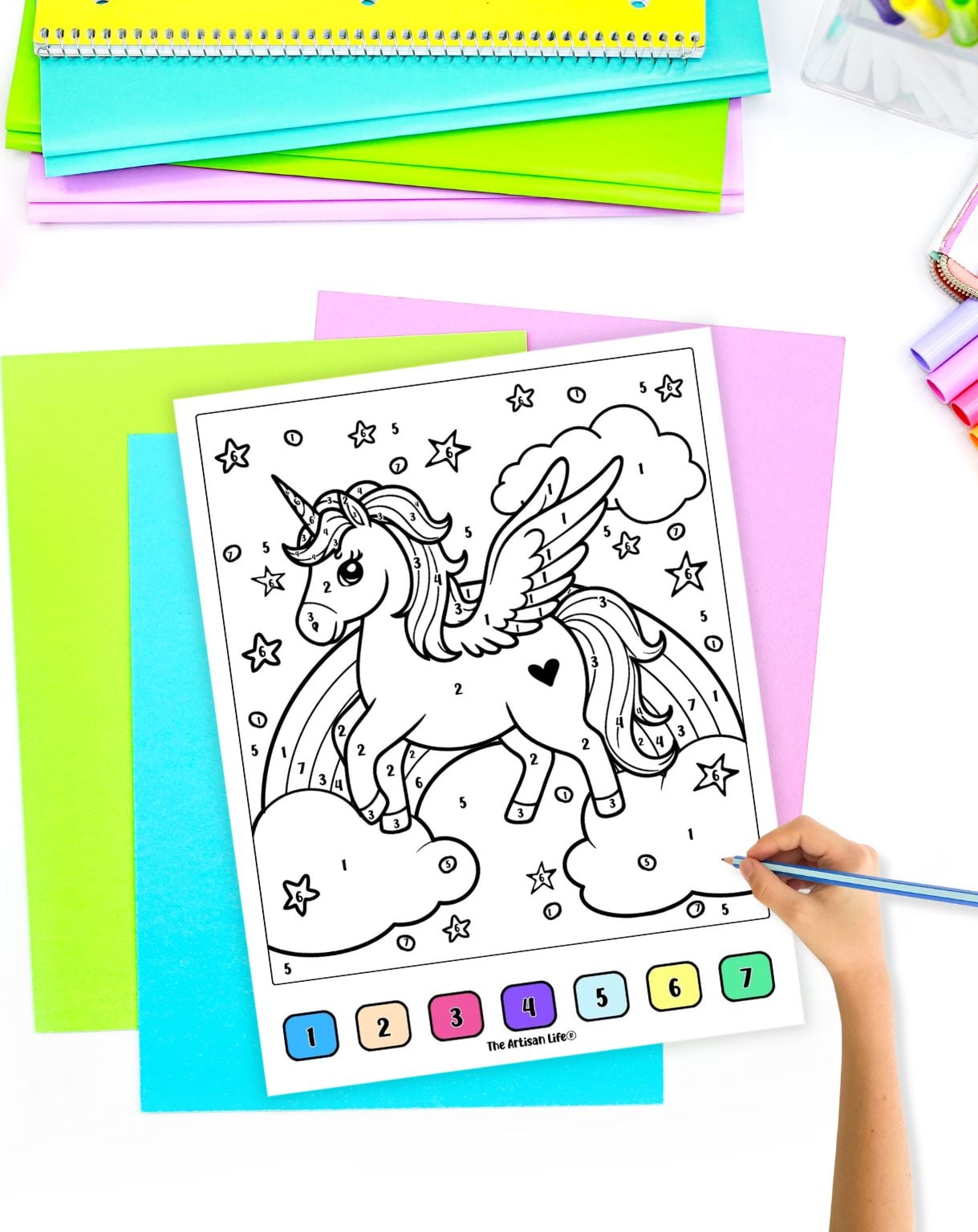 a hand with a blue pencil preparing to color a unicorn themed color by number worksheet