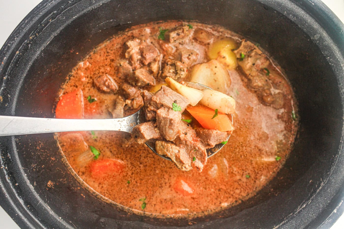 lifting a spoon full of beef stew from a slow cooker crock