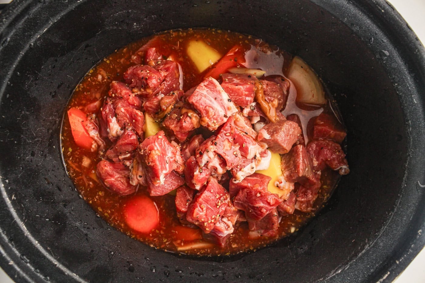 uncooked beef stew in a. slow cooker crock