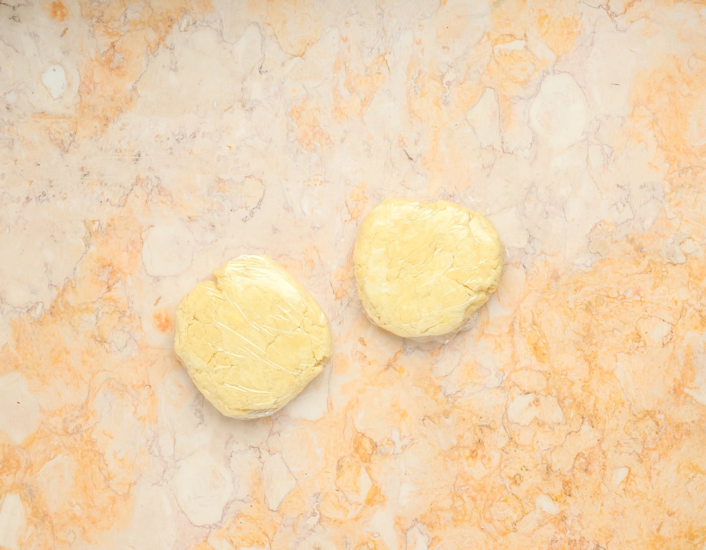 two pie crust dough balls in plastic wrap