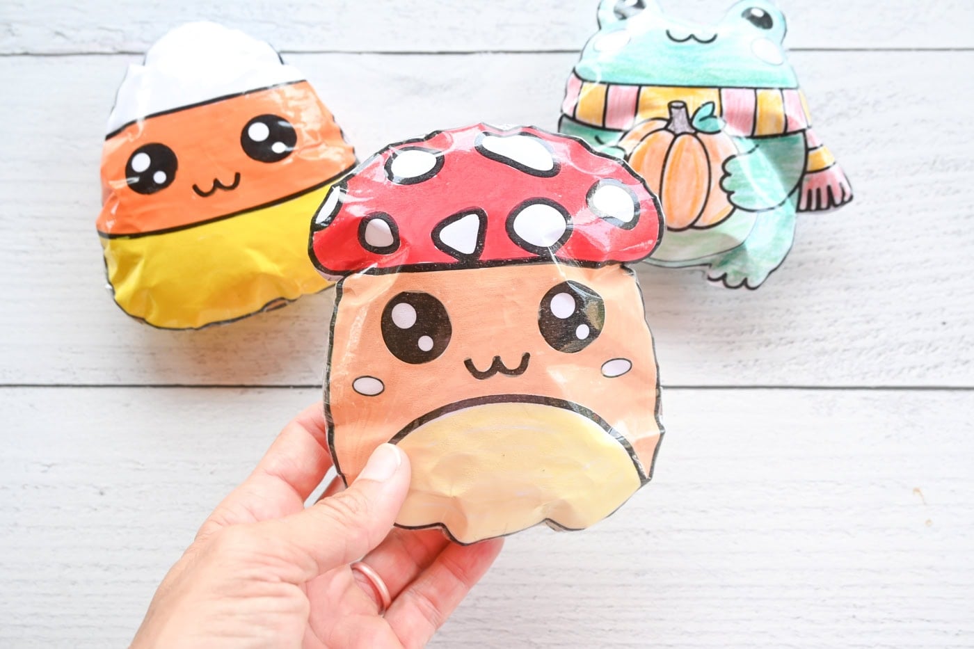 holding a mushroom paper squishy in front of a candy corn squishy and a cute frog squishy