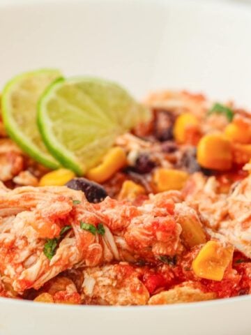 a close up of a plate with slow cooker salsa chicken and limes
