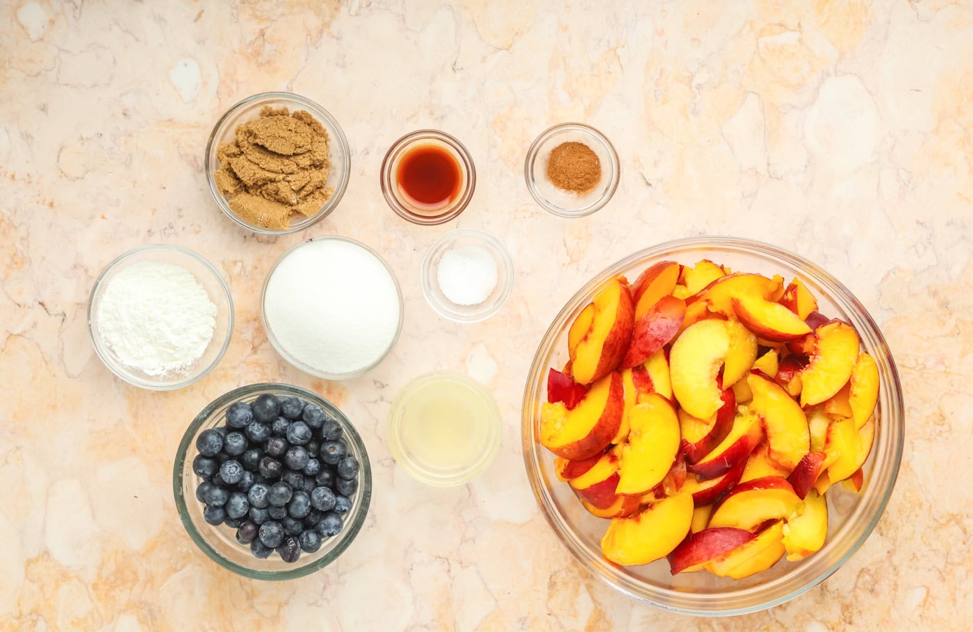 ingredients for fresh peach pie filling including peaches, sugar, and blueberries