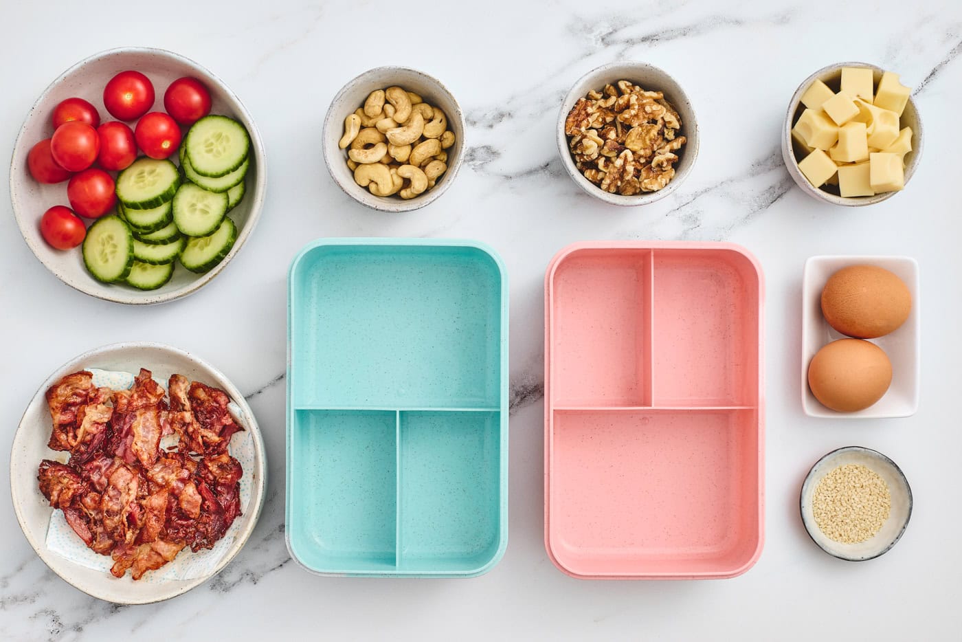 two empty bento lunboxes surrounded by veggies, eggs, and nuts