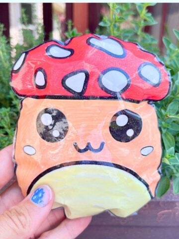 a hand holding a paper mushroom squishy in front of a box of herbs