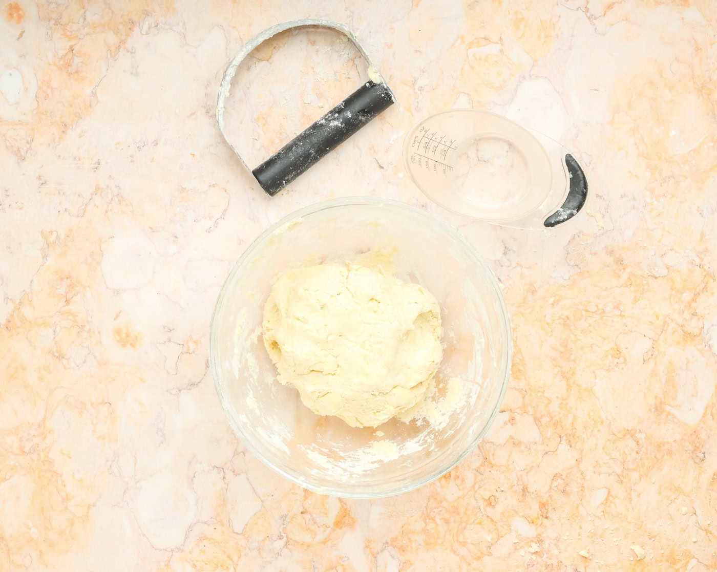 pie crust in a bowl next to a pastry cutter