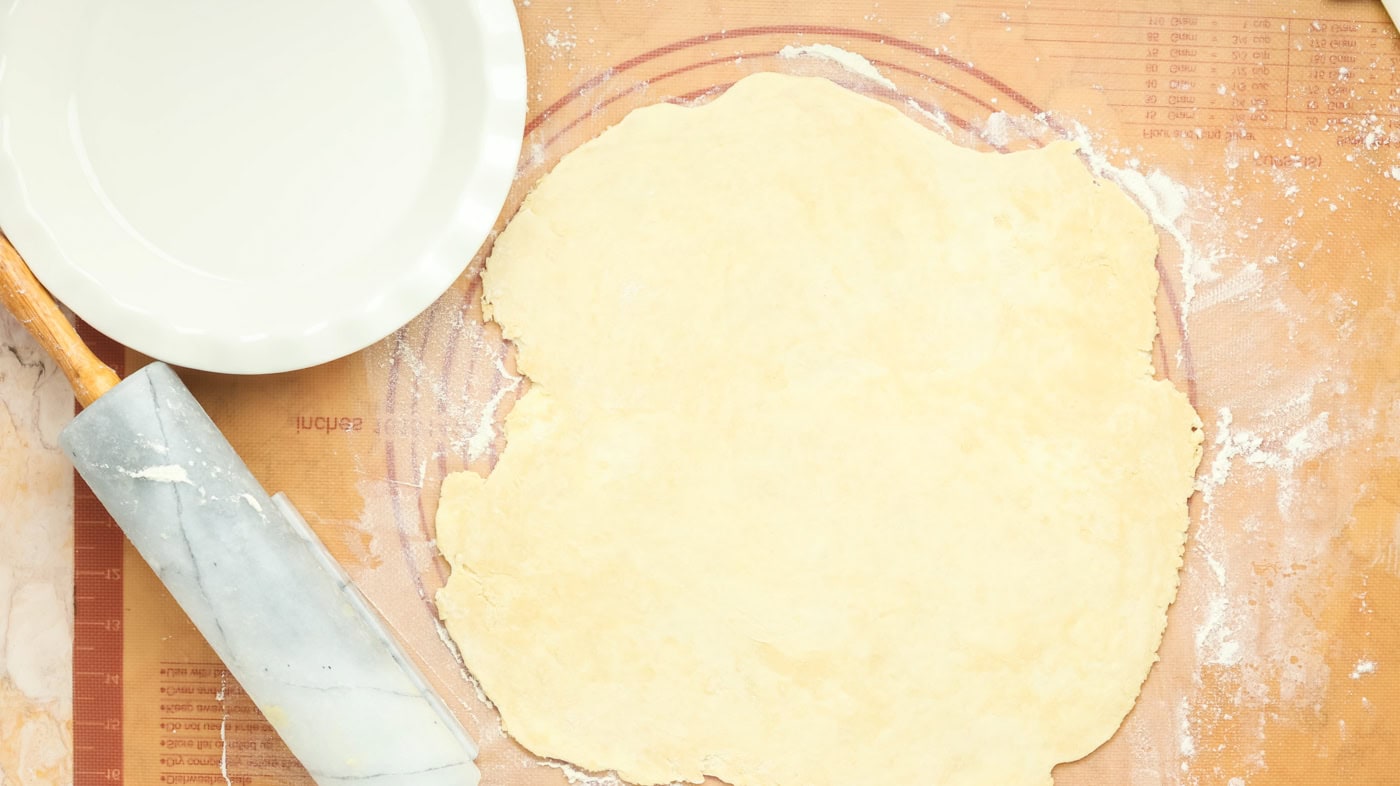 a ball of pie crust dough on a dough rolling mat rolled into a circle