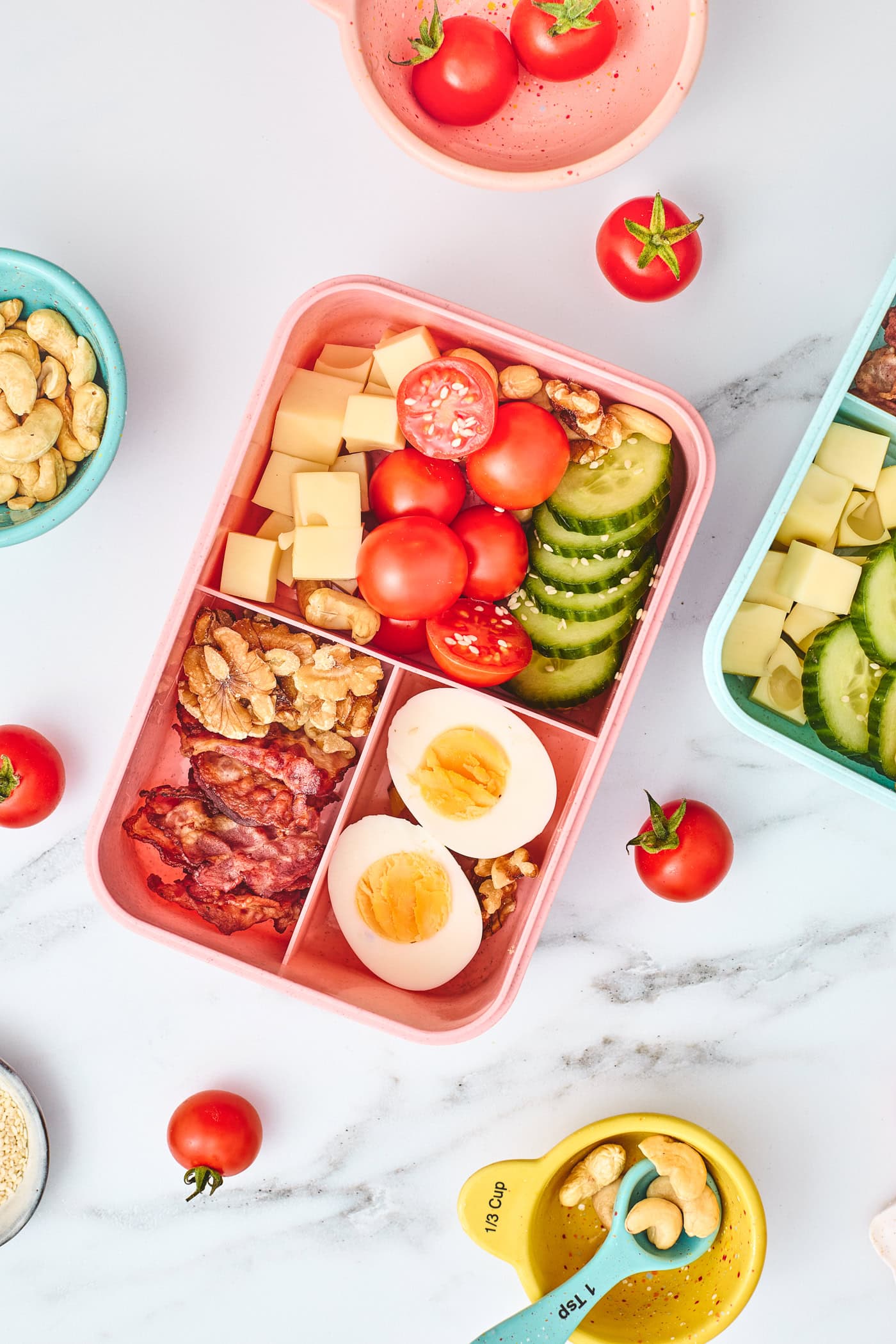 a top down vertical photo of a child's bento lunchbox with bacon, eggs, veggies, and nuts