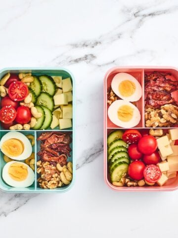 a top down vertical photo of two child's bento lunchbox with bacon, eggs, veggies, and nuts