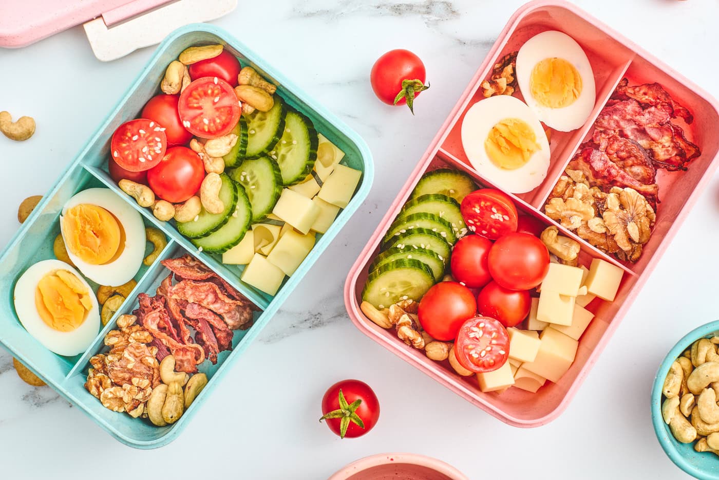 a top down photo of two bento style lunchboxes for kids. Each one has savory, high protein options like eggs, nuts, and cheese
