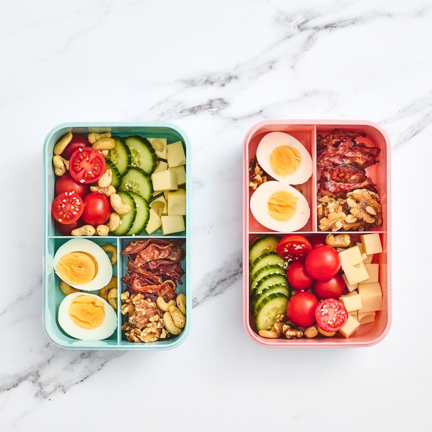 a top down vertical photo of two child's bento lunchbox with bacon, eggs, veggies, and nuts