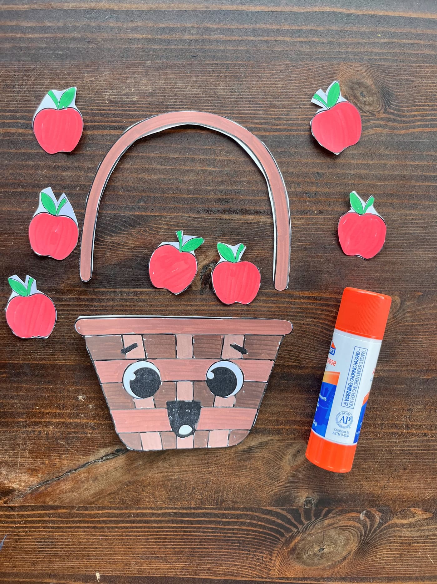 cut out pieces of a. cute apple basket craft for kids shown alongside a glue stick