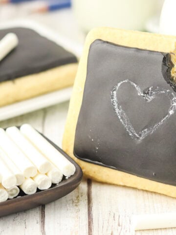 chalkboard sugar cookies with a cookie with a bite taken out of it leaning against a glass bottle of milk