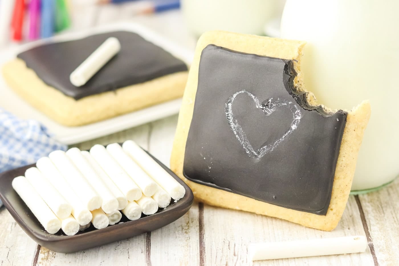 chalkboard sugar cookies with a cookie with a bite taken out of it leaning against a glass bottle of milk