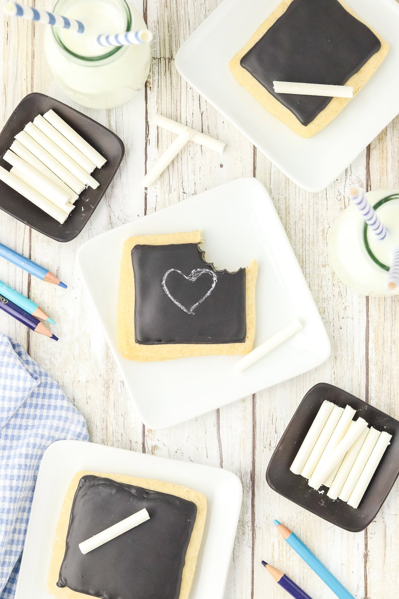 a top down view of chalkboard sugar cookies with edible chalk on square white plates