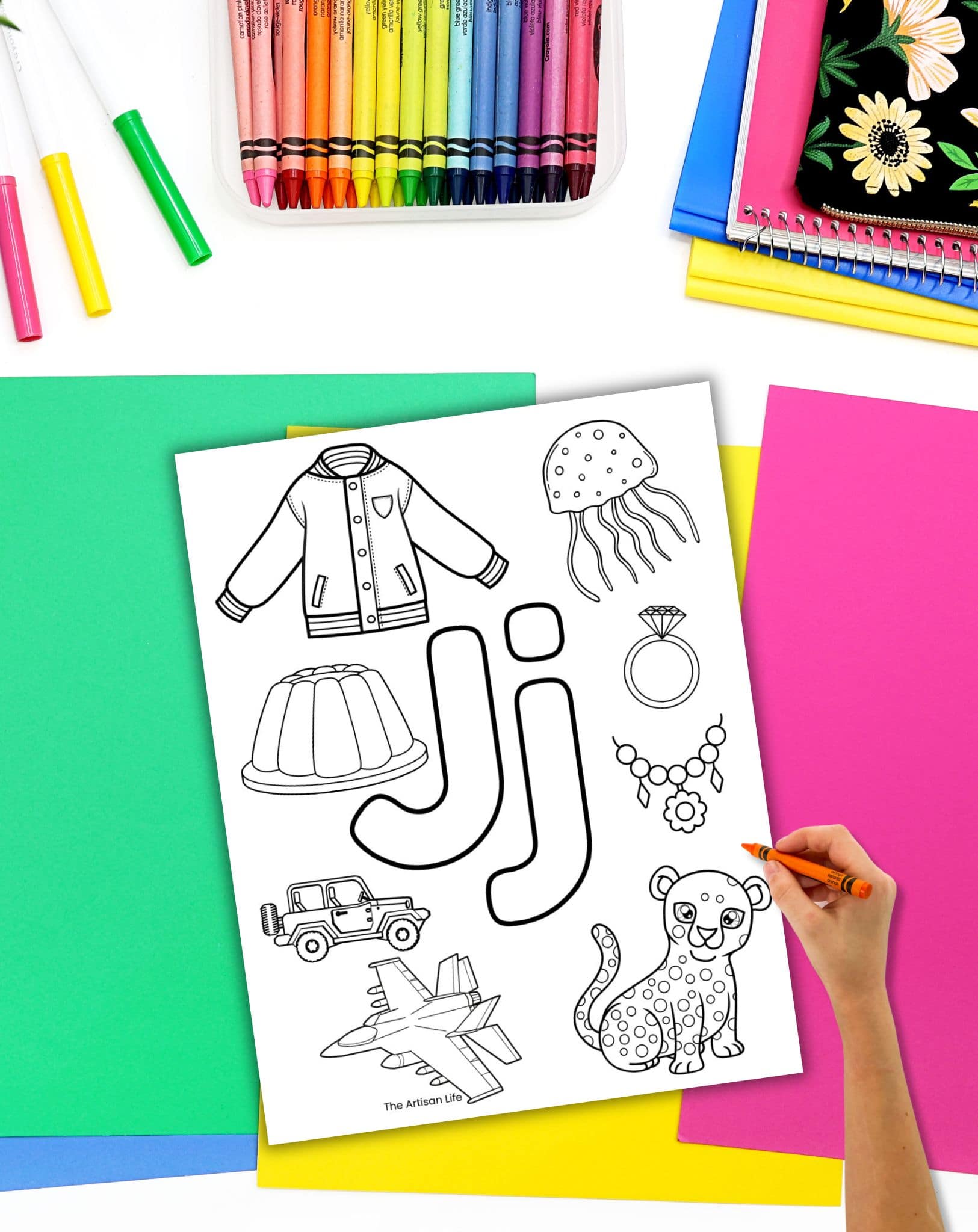 A hand with a crayon preparing to color a j themed alphabet coloring page