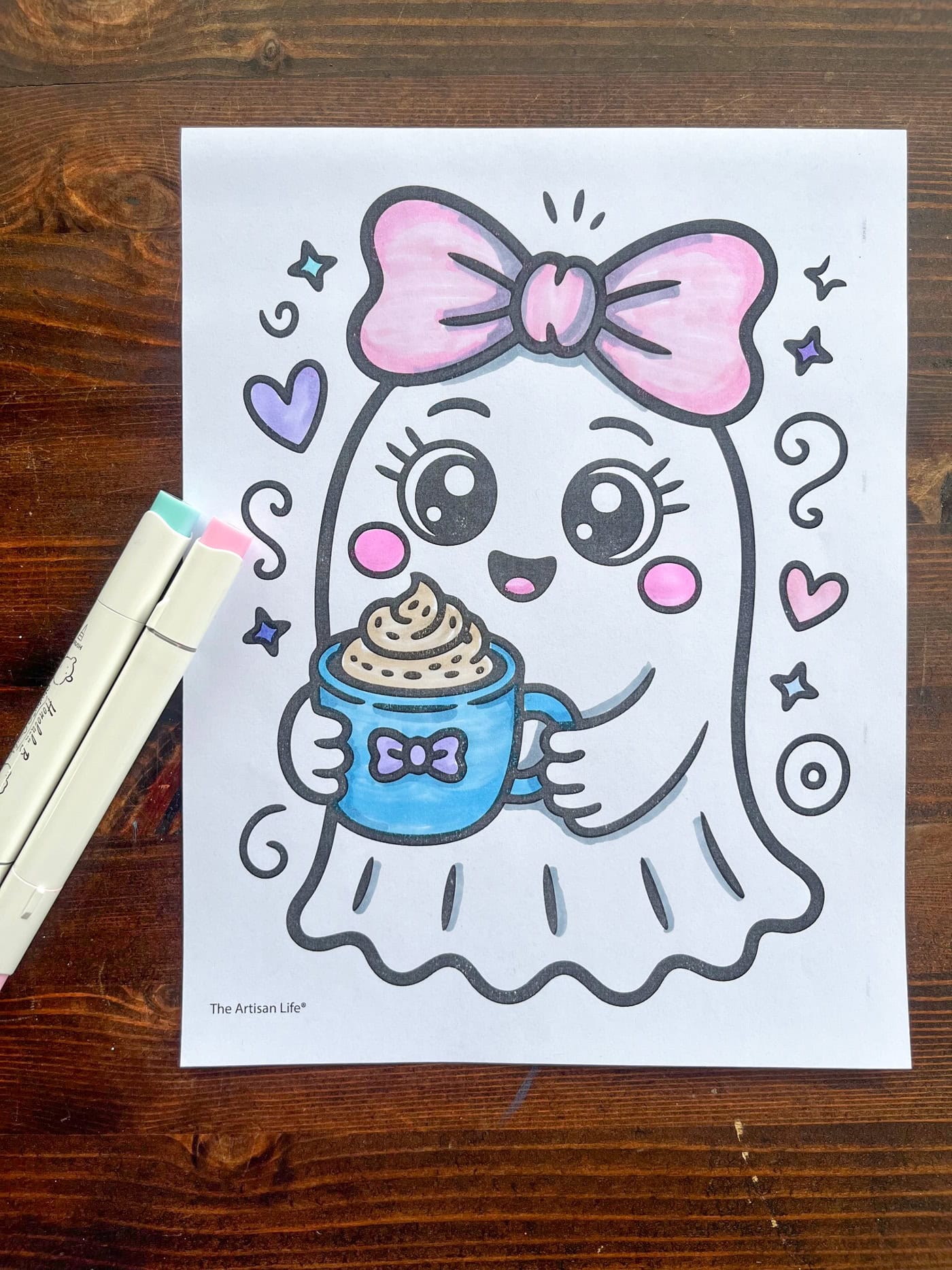 a top down photo of a ghost coloring page colored with alcohol markers next to a pink marker and a blue marker