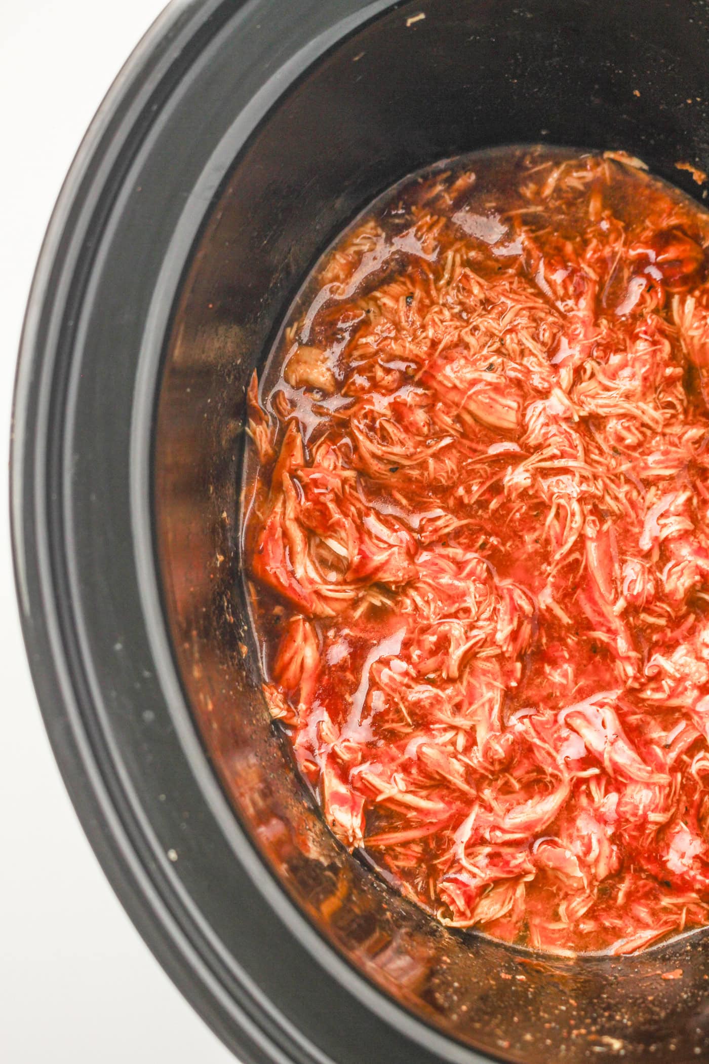 a top down photo of shredded slow cooker honey bbq chicken in a slow cooker crock