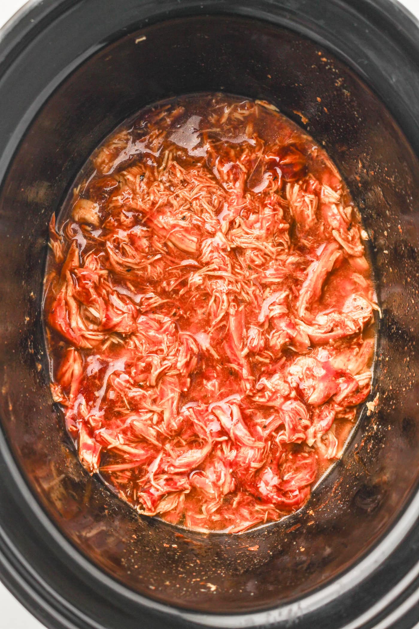 a top down photo of shredded slow cooker honey bbq chicken in a slow cooker crock