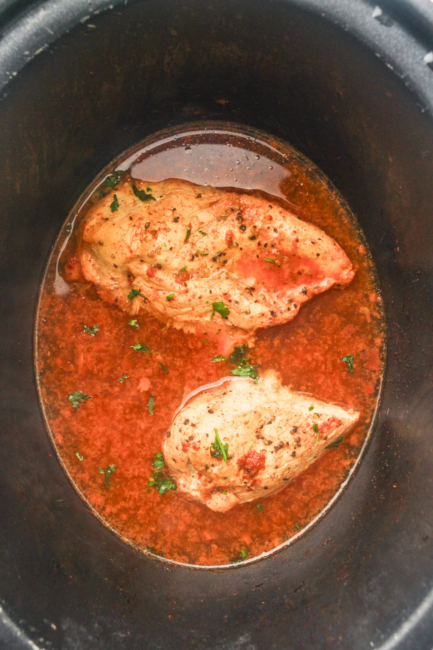 a top down photo of two cooked chicken breasts with sauce in a slow cooker crock for honey bbq chicken