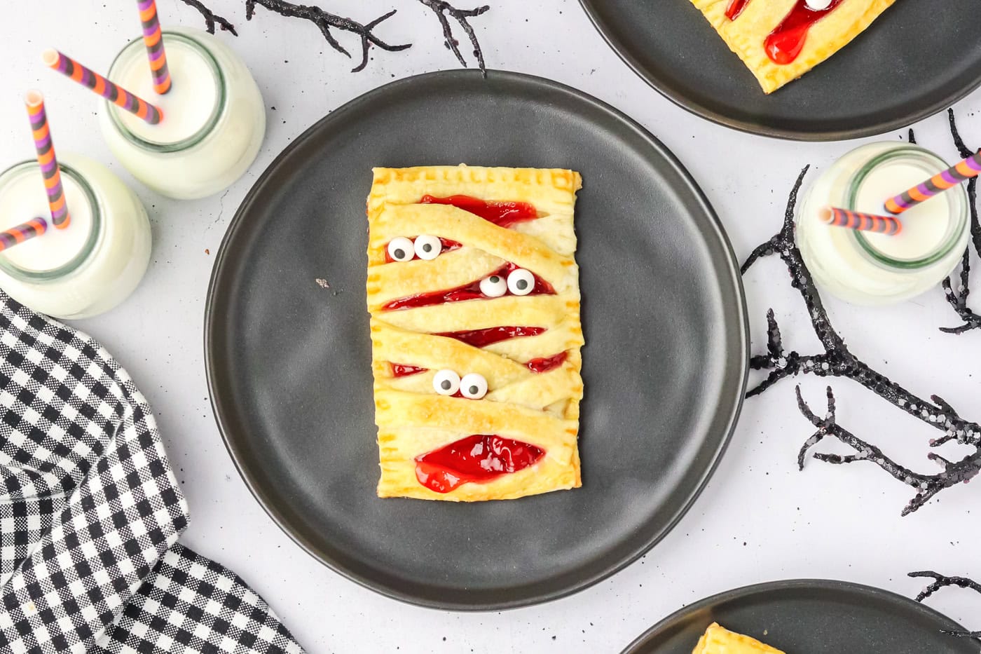 a mummy puff pasty for halloween with eyeballs to look like a mummy. It is on a black plate.