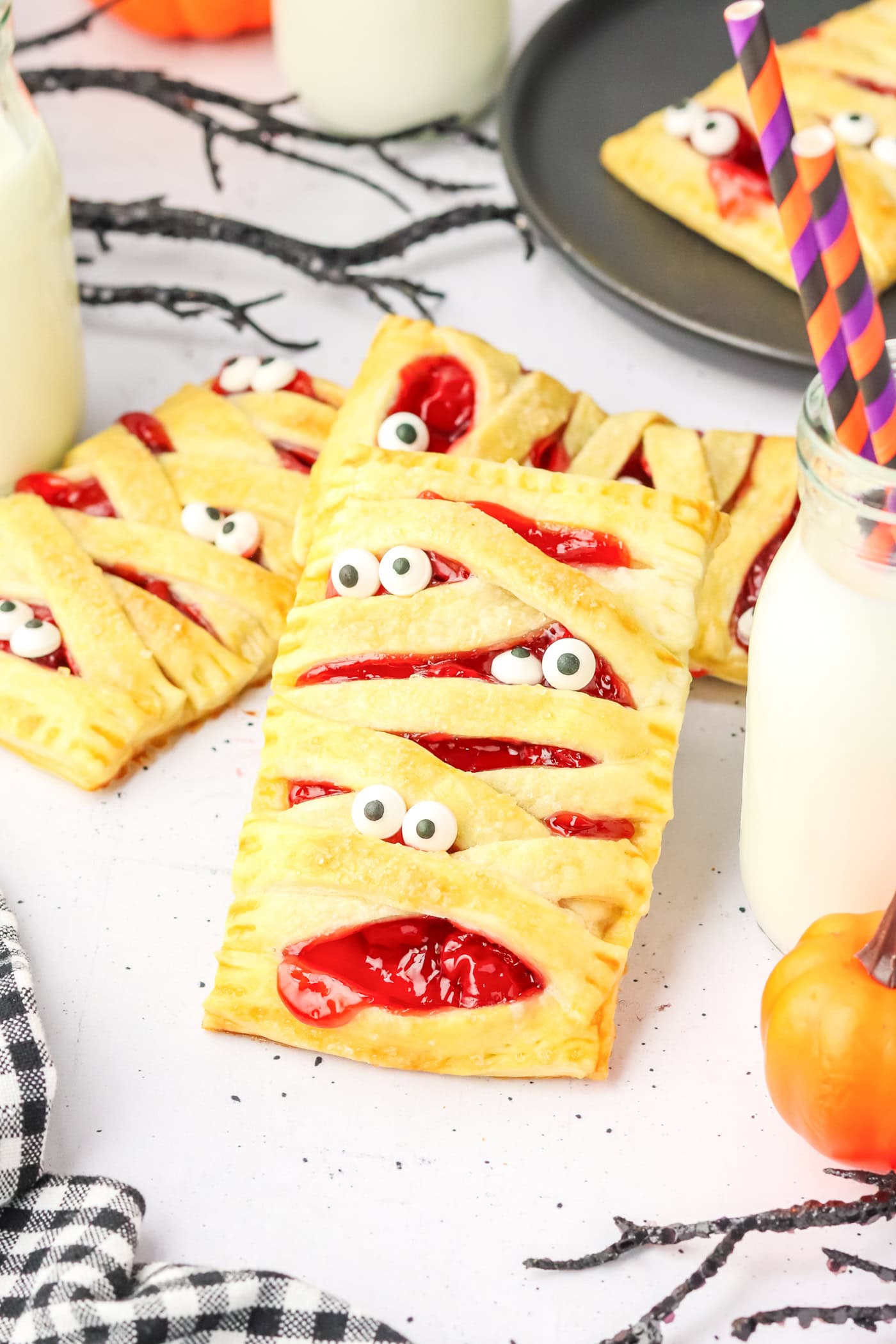 a counter with mummy puff pastries with eyeballs. small pumpkins and twigs are visible along the edges of the photo