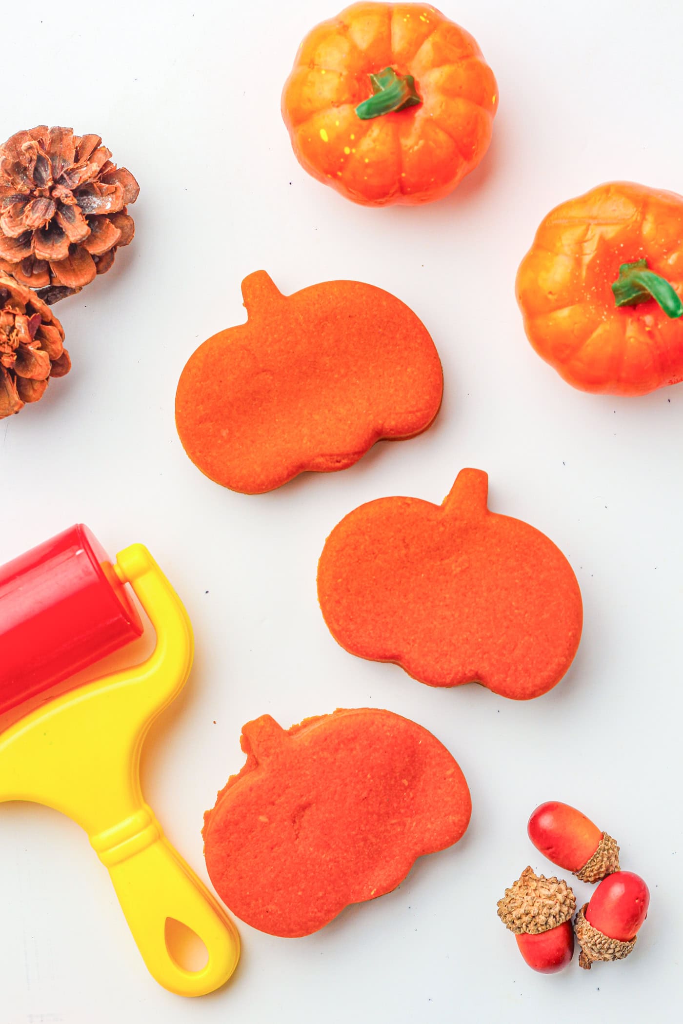 a top down photo of three pumpkin play dough shapes with a play dough roller