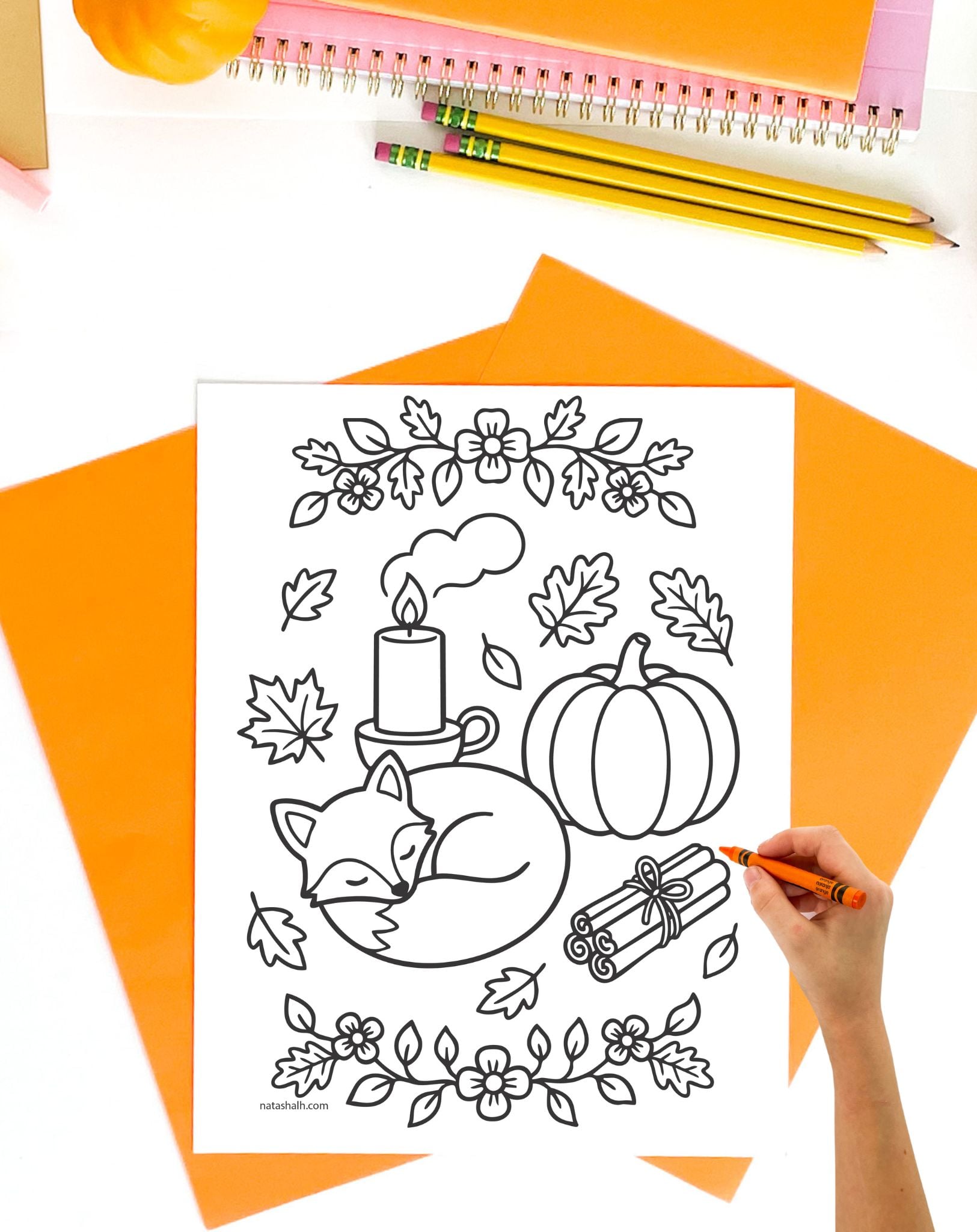 a hand coloring a fall coloring sheet with a fox, a pumpkin, and a candle