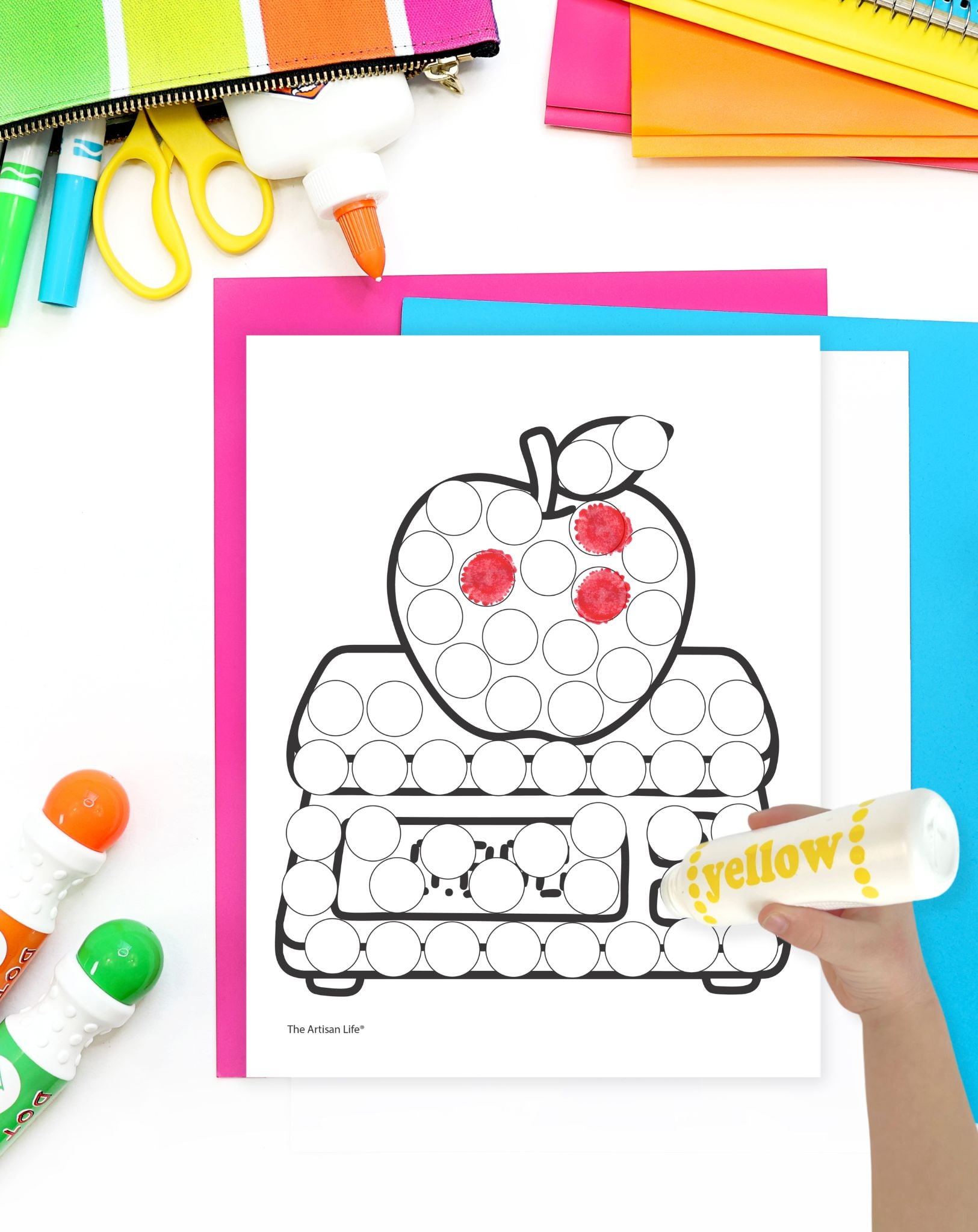 a hand with a yellow dot marker coloring a dot marker coloring sheet with an apple on a grocery scale
