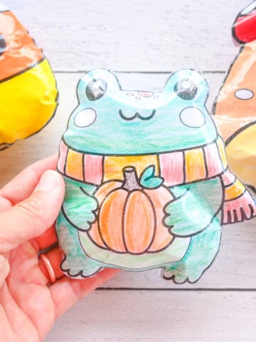 a hand holding a paper frog squishy. A mushroom and candy corn squishy are seen in the background