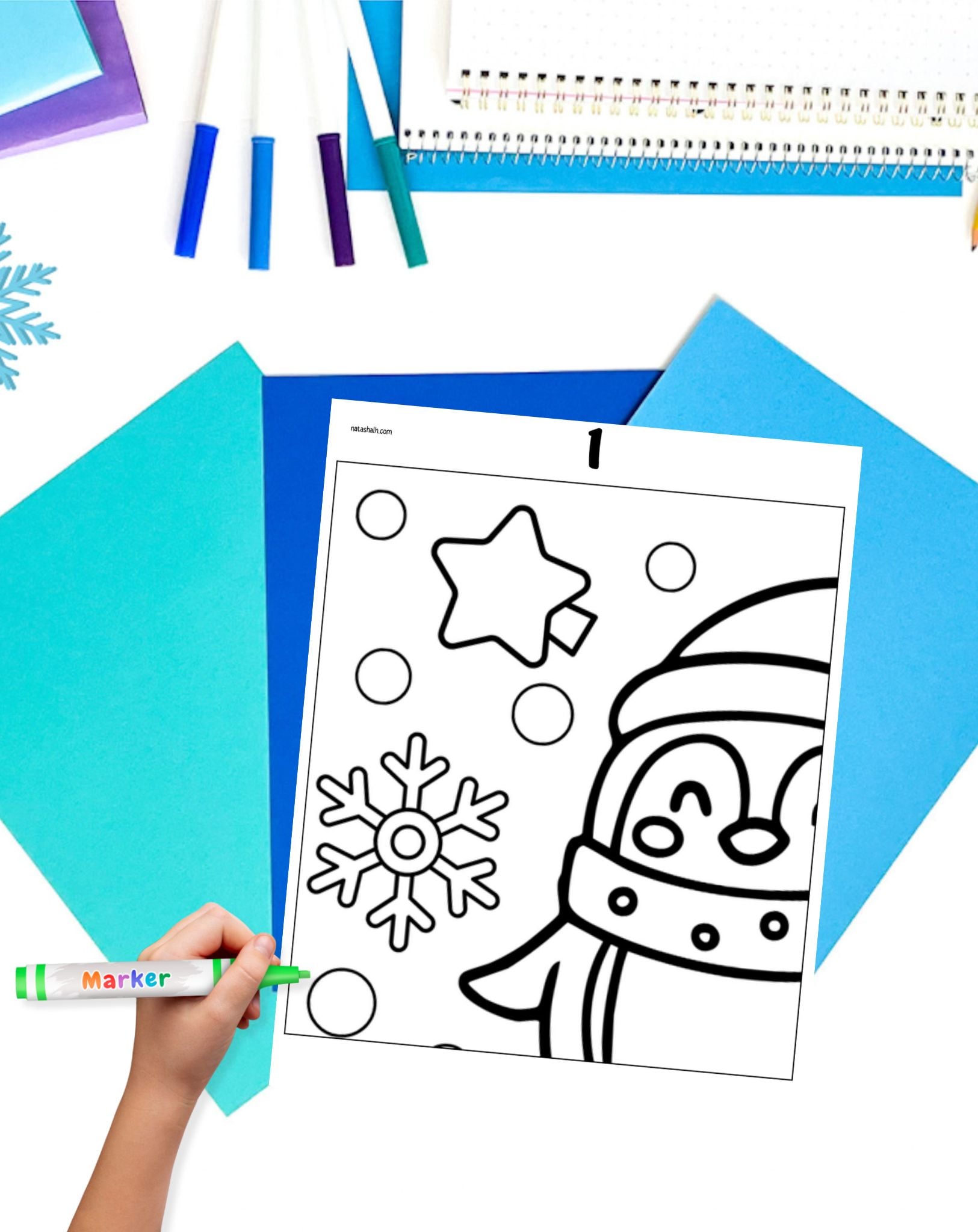 a child's hand with a maker preparing to color a penguin and snowflake coloring page that is part of a large collaborative poster